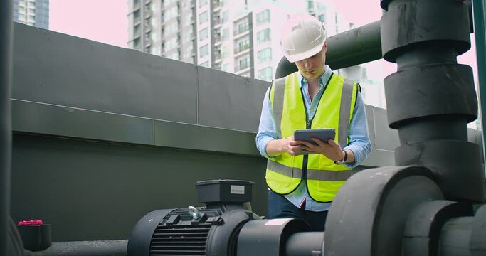A Engineer man looking inspecting maintenance insulated pipelines valve pump control on the roof at an industrial site. He is wearing a hard hat and safety vest	
