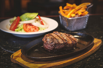 Juicy beef steak accompanied by fries sweet potato and fresh salad.