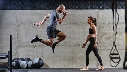 A fit couple exercising various types of jumps in a modern gym, demonstrating their physical...