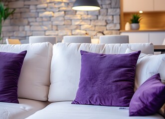 Modern living room interior with a white sofa, purple pillows and decorative stone wall paneling on the walls, a dining table in the background