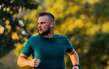 Young athletic man running or jogging at the park listening to music on wireless headphones active...