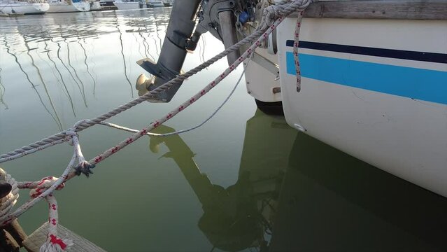 back of a yacht with an outboard motor tied to with ropes to a mooring slightly rocking as the water moves below.