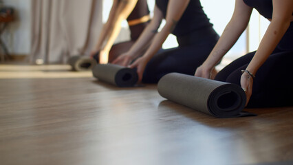 Close up of female sports group rolling mats to start pilates. Media. Beginning of exercises and...