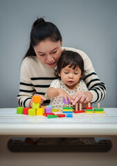 mother teaching her toddler baby girl to playing wooden educational geometric on table