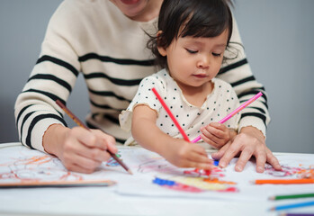 toddler baby training to drawing with colored pencil with mother helping on table