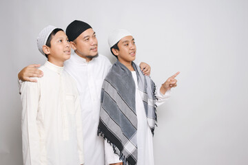 Asian Muslim Father With His Sons Looking And Pointing Aside To The Empty Space For Ads Or Text