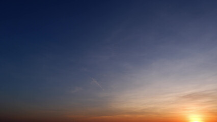 A serene sunrise with a gradient sky transitioning from deep blue at the top to soft orange and yellow hues near the horizon, with the sun just peeking over. Sunrise sky background.
