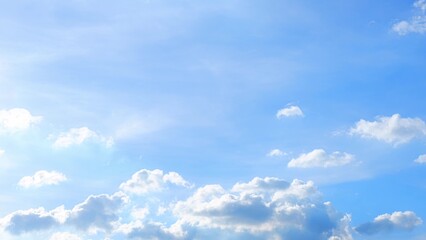 A bright, clear blue sky with scattered, fluffy white clouds. The sunlight softly illuminates the...