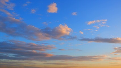 Obraz premium A serene sunset sky with scattered clouds reflecting warm tones of orange and pink. The deep blue sky contrasts beautifully with the soft colors of the clouds, creating a tranquil scene. 