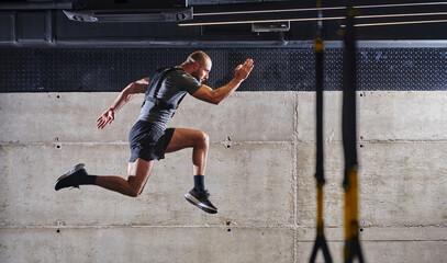 A muscular man captured in air as he jumps in a modern gym, showcasing his athleticism, power, and...