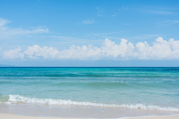 Sandy beach with rolling calm wave of ocean on sunny day on background white clouds in blue sky