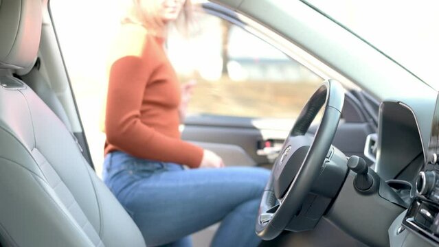 Woman in an orange sweater gets into the car and fastens her seatbelt. She is seen pulling the seatbelt across her body, ensuring safety before driving.
