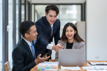 A group of three business professionals collaborating on a project with a laptop in a modern office setting, discussing ideas enthusiastically.
