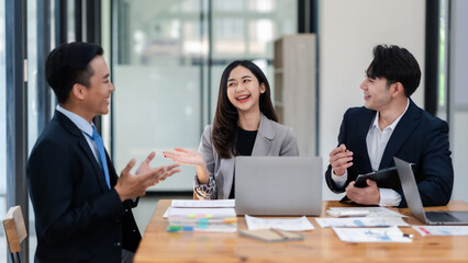 Business professionals engaging in a cheerful discussion during a meeting in a modern office setting with laptops and documents.