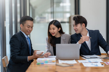 Business team discussing project in modern office, analyzing documents on laptop. Professional collaboration and teamwork concept.