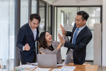 Three business professionals celebrating success at the office with a high-five, showing excitement and teamwork.