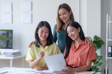 Three happy young Asian businesswomen working together in a bright office environment, reviewing documents and smiling with a positive attitude.