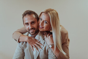 A business couple posing for a photograph together against a beige backdrop, capturing their...