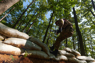 An elite soldier adeptly clears military barriers in the perilous wooded terrain, showcasing...