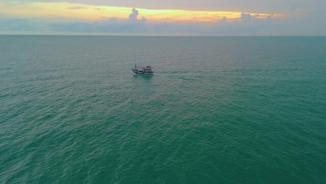 Aerial view small fishing boat trawler sails along the sea surface at sunset for night seafood fishing.