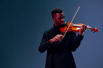 Elegant man in black suit playing violin on dark background in atmospheric setting with dramatic...