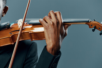 Elegant African American man playing the violin in a tuxedo on a gray background