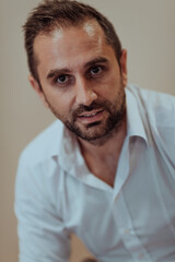 Obraz premium A confident businessman sitting while a beige background enhances the professional atmosphere, showcasing his productivity and expertise.
