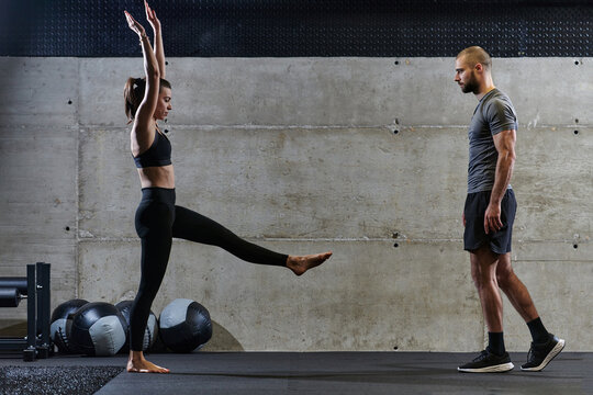 A muscular man assisting a fit woman in a modern gym as they engage in various body exercises and muscle stretches, showcasing their dedication to fitness and benefiting from teamwork and support
