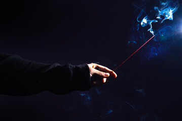 Mano, sosteniendo una varilla de incienso, en fondo negro con humo iluminado.