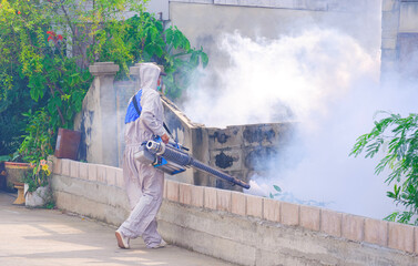 Healthcare worker in protective clothing is spraying chemical to eliminate mosquitoes in overgrown area next to the old house