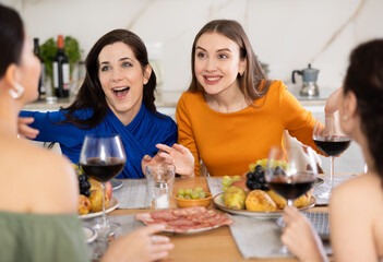Happy women congregated around a festive table; participating in animated discussions and enjoying the delights of red wine