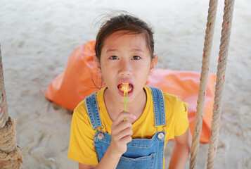 Close up of Asian girl eating French fries with dip cheese while sitting on swing at the beach.