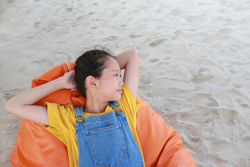 Asian young girl in dungarees jean looking beside and relax on orange sofa bed beach on sand at...