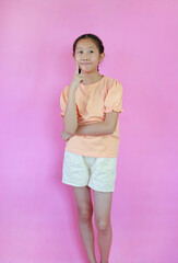 Funny face Asian girl kid hold finger cheek while standing isolated on pink studio background.