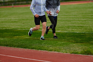 Fototapeta premium An inspiring and active elderly couple showcase their dedication to fitness as they running together on a lush green field, captured in a close-up shot of their legs in motion.