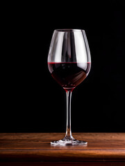 Glass of red wine on black background and on a wooden desk