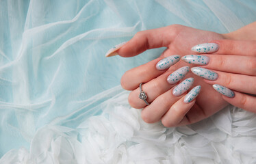 Female hands with blue nail design on blue silk background.