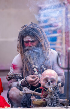 Portrait of an naga aghori sadhu holy man with pyre ash on his face and body performing aghor sadhna and smoking at harishchandra ghat in varanasi.	
