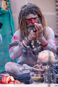 Portrait of an naga aghori sadhu holy man with pyre ash on his face and body performing aghor sadhna and smoking chilam at harishchandra ghat in varanasi.	
