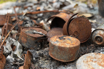 Old, rusted metal cans in burned ash. Trash in abandoned army base, burned, rusty.