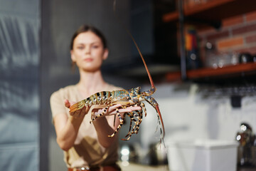 Woman holding a large lobster in a kitchen setting with a sink in the background, preparing seafood...