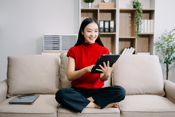 Obraz premium Young asian woman using smartphone and tablet while seated on couch at home
