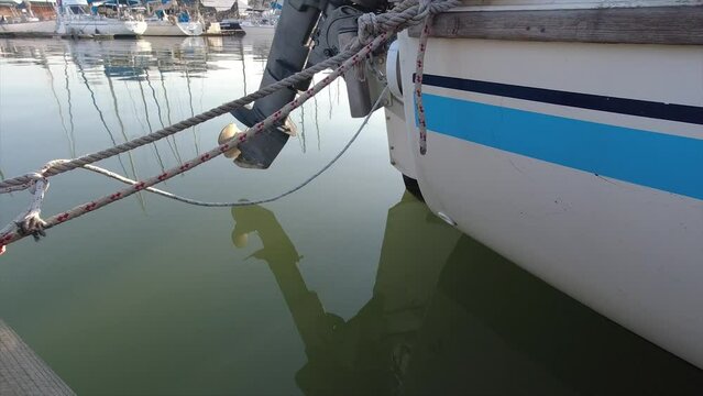 back of a yacht with an outboard motor tied with ropes to a walk-on mooring slightly rocking as the water moves below in a marina club