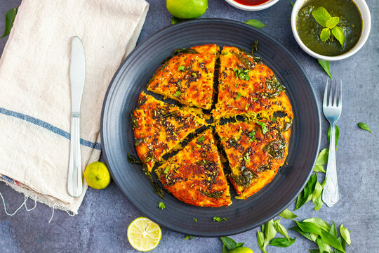 selective focus of Gujrati dish handvo slice tringle cut decorated with lemon, curry leaves, mint chutney and tomato sauce.