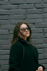 Stylish attractive young woman wearing black coat with glasses. Female model posing. High quality photo