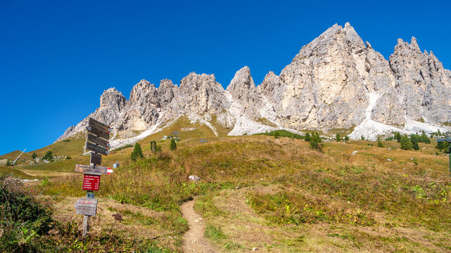 Magical Dolomite peaks of Pizes da Cir, Passo Gardena at blue sky and sunny day with a post sign trailhead showing a walking man, South Tyrol, Italy.