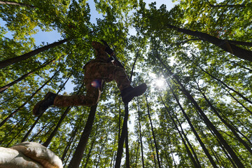 An elite soldier adeptly clears military barriers in the perilous wooded terrain, showcasing...