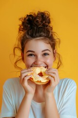 Young woman with a messy bun enjoying a powdered doughnut, smiling broadly on a yellow background