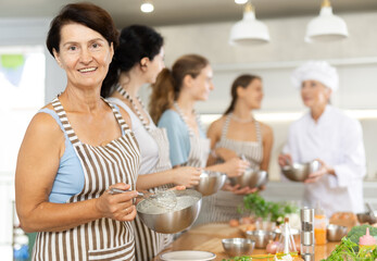 Senior lady while studying at culinary workshop school, cooks appetizing sauce, marinade, dough in bowl.