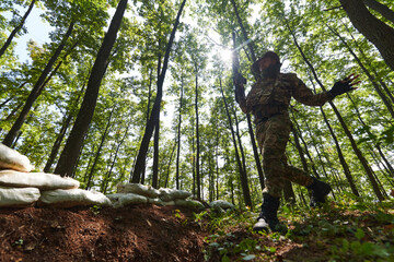 An elite soldier adeptly clears military barriers in the perilous wooded terrain, showcasing tactical skill and agility during specialized training